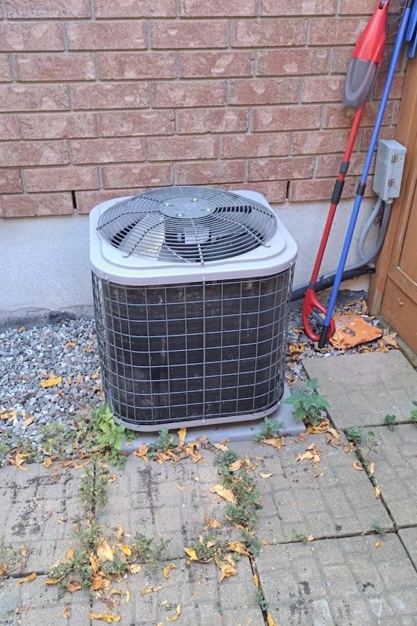Une unité extérieure de thermopompe de forme cubique moderne, posée sur une dalle de béton à côté de la maison.