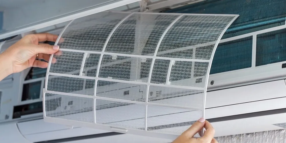 Une personne réinsère un filtre à tamis propre et translucide dans le climatiseur après l'avoir lavé et séché.