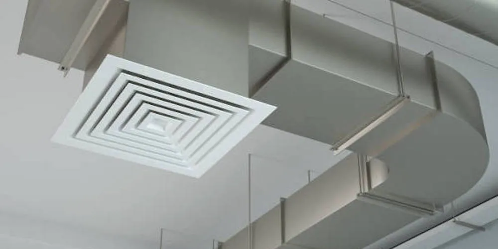 Vue en contre-plongée d'un diffuseur de plafond carré blanc relié à un conduit de ventilation rectangulaire en acier galvanisé avec un coude à 90 degrés.