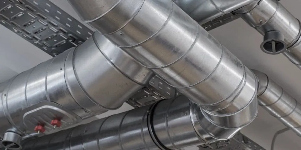 Gros plan sur plusieurs conduits métalliques cylindriques à spirale installés parallèlement, montrant une jonction en T et des chemins de câbles métalliques au-dessus.