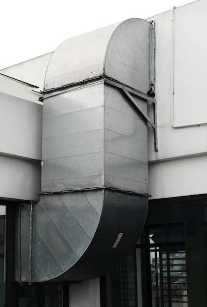 Un imposant système de conduits verticaux en acier galvanisé monté sur la façade extérieure d'un bâtiment blanc, comprenant deux larges sections courbes à 90 degrés.